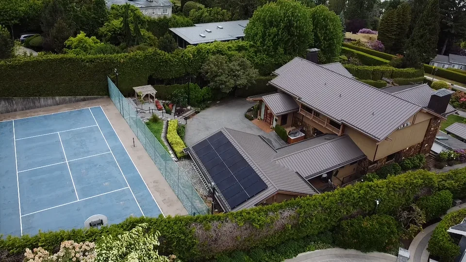 Aerial view of a solar array on the metal roof of a large Richmond home beside a tennis court