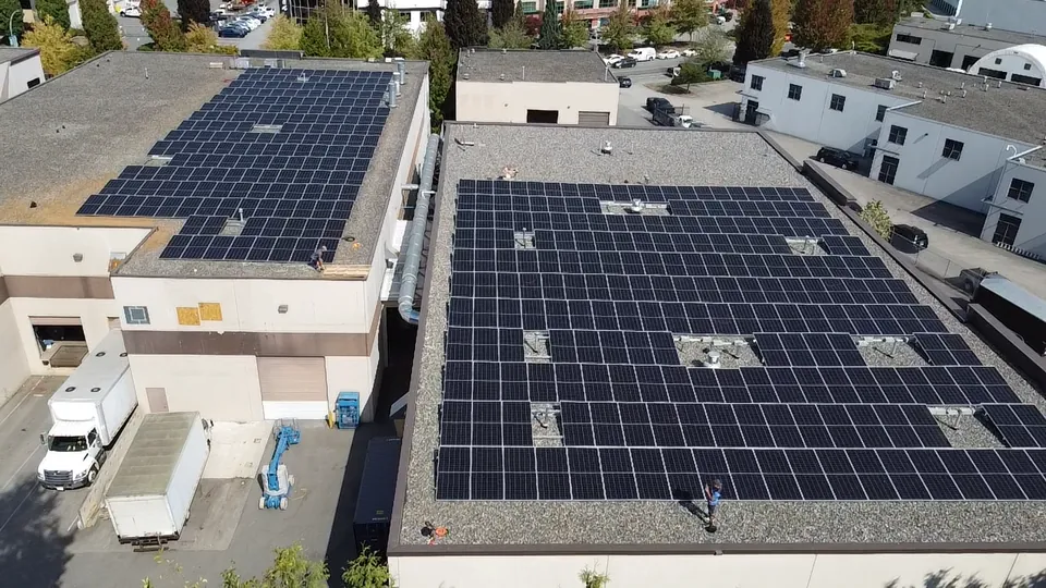 Aerial view of large solar arrays across the flat gravel roofs of two commercial buildings