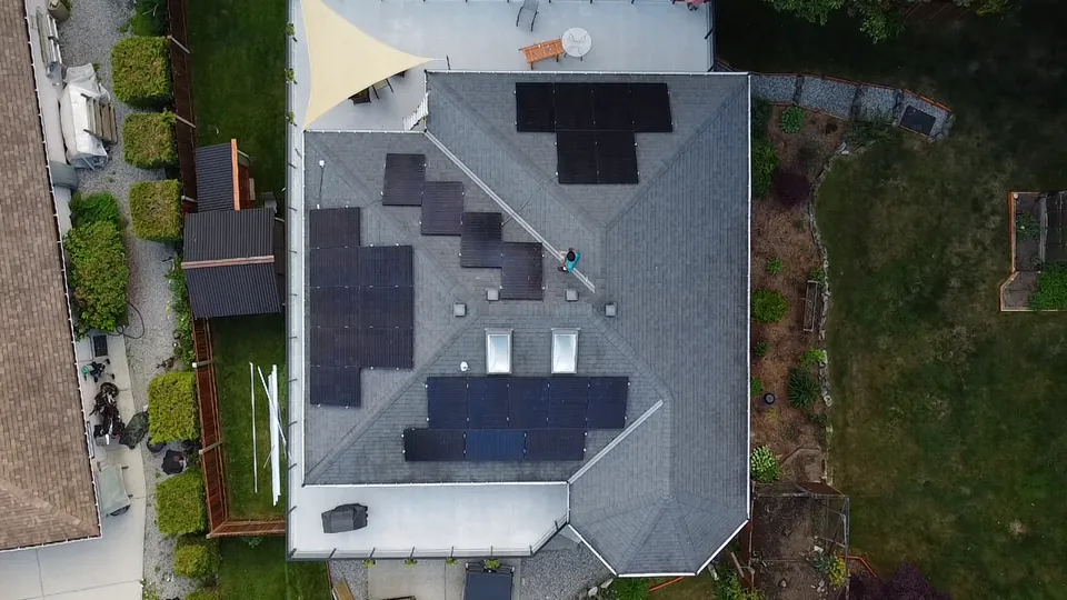 Top down drone view of black solar panels on a hipped shingle roof, with an installer on the roof
