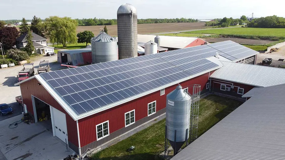 Solar array on the roof of a red farm building beside grain silos