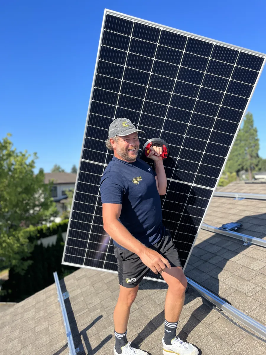A Pure Solar installer carrying a solar panel across a residential roof on a clear day