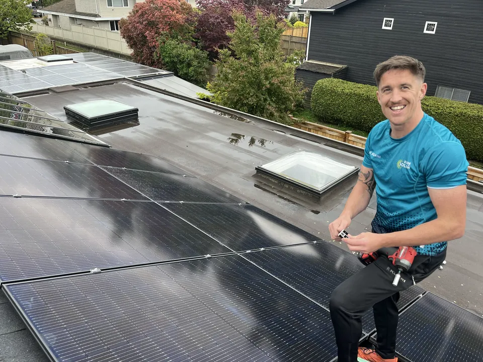 A Pure Solar installer kneeling beside black solar panels and skylights on a flat residential roof